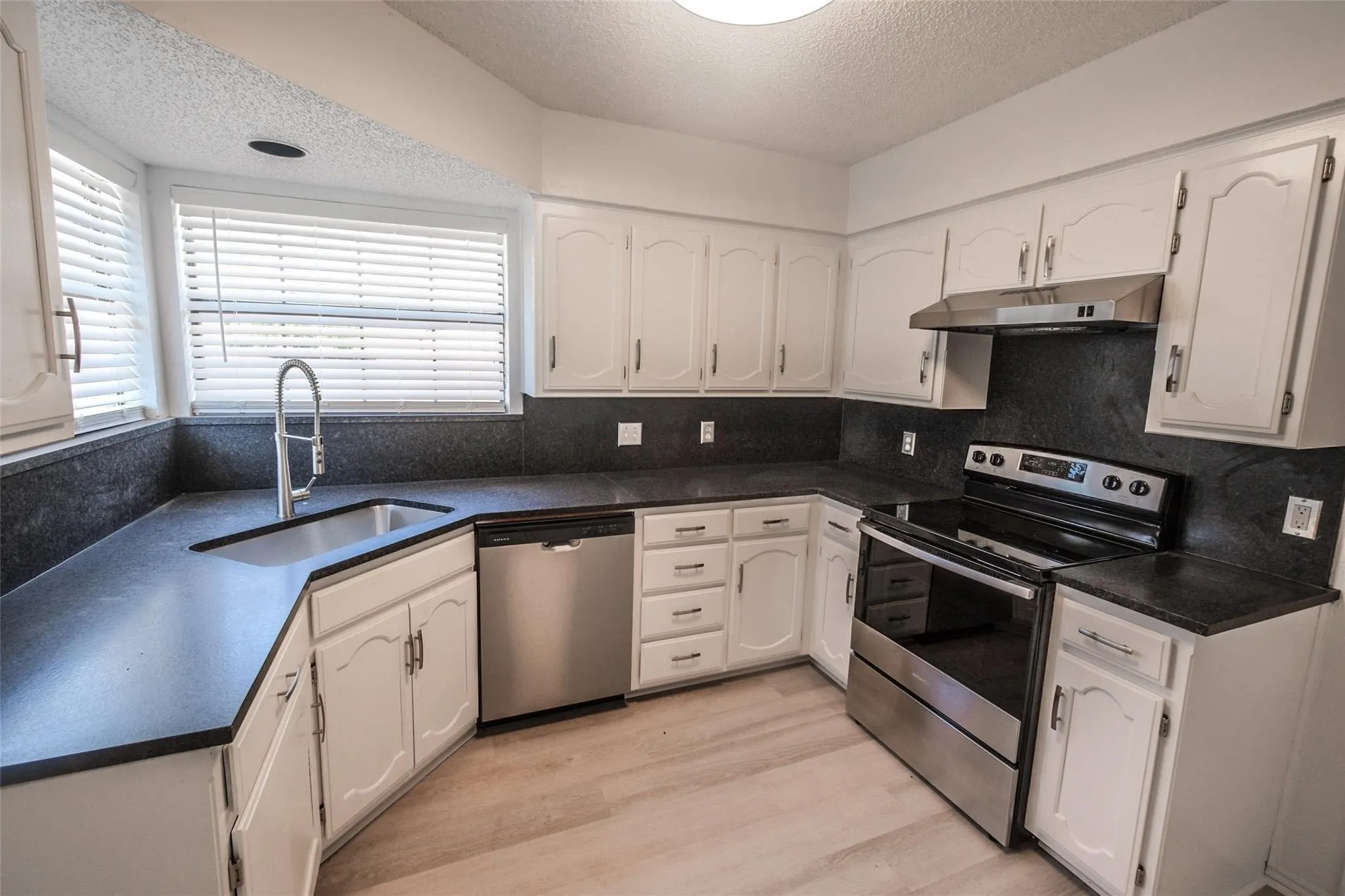 White cabinetry with dark countertops, stainless steel appliances, and wood-finish flooring