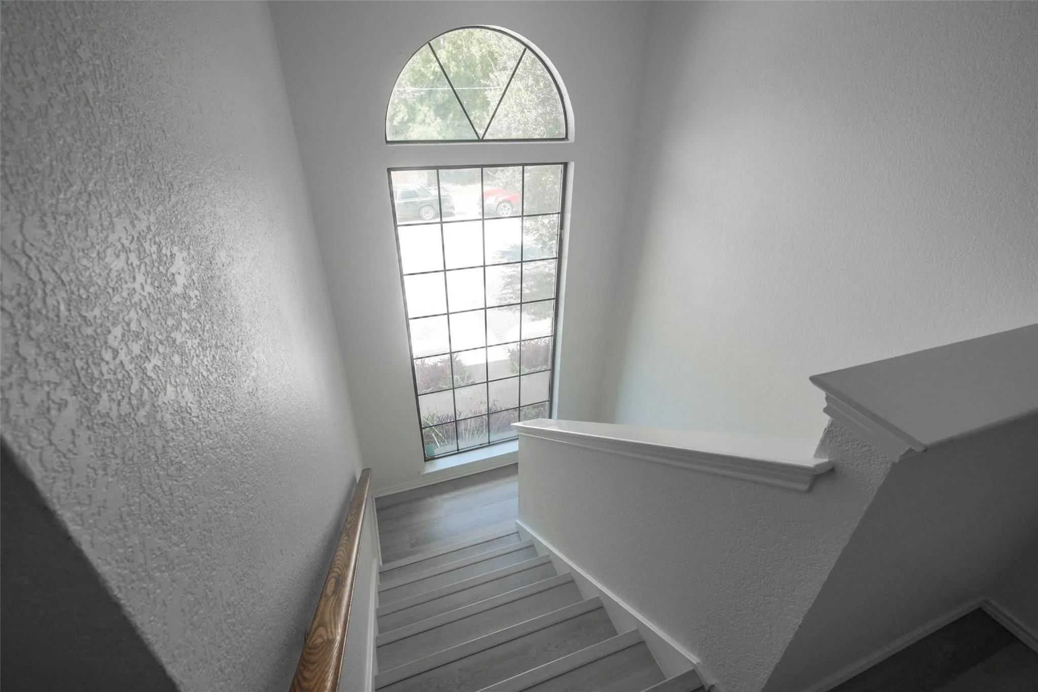 Staircase featuring wood-finish treads, a large arched window, and textured walls