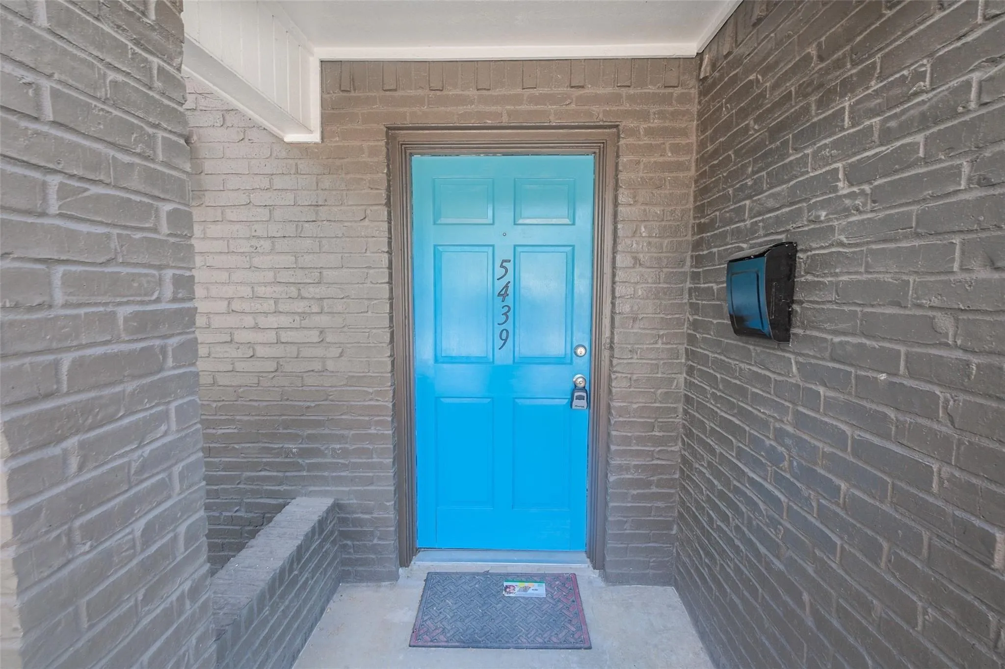 Entryway featuring gray brick and a bright blue paneled door with house numbers