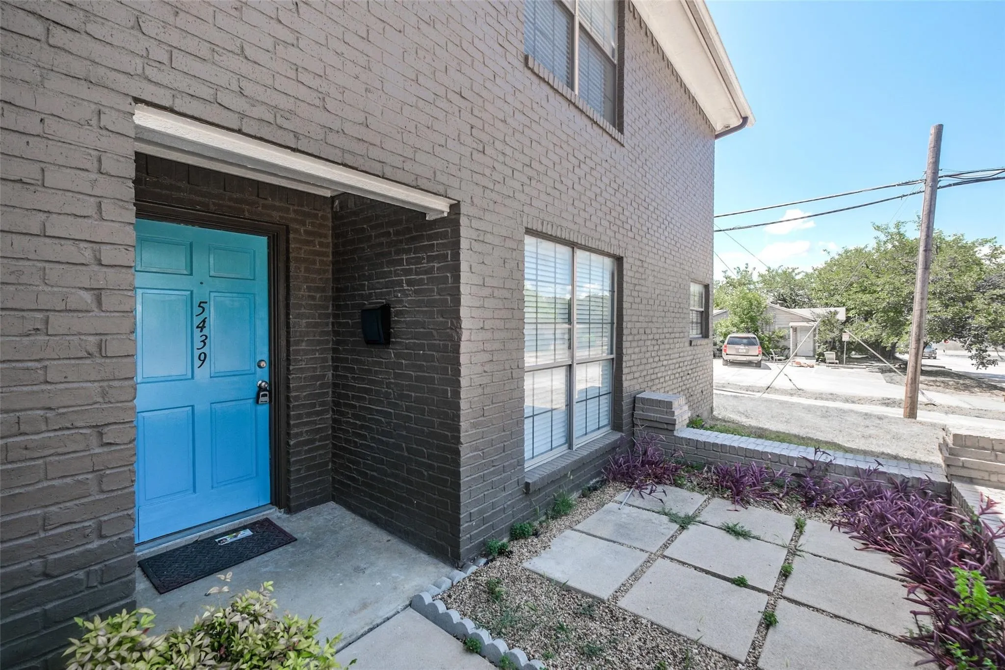 Brick exterior facade, bright blue entry door, concrete stepping stones, low-maintenance landscaping, and window blinds