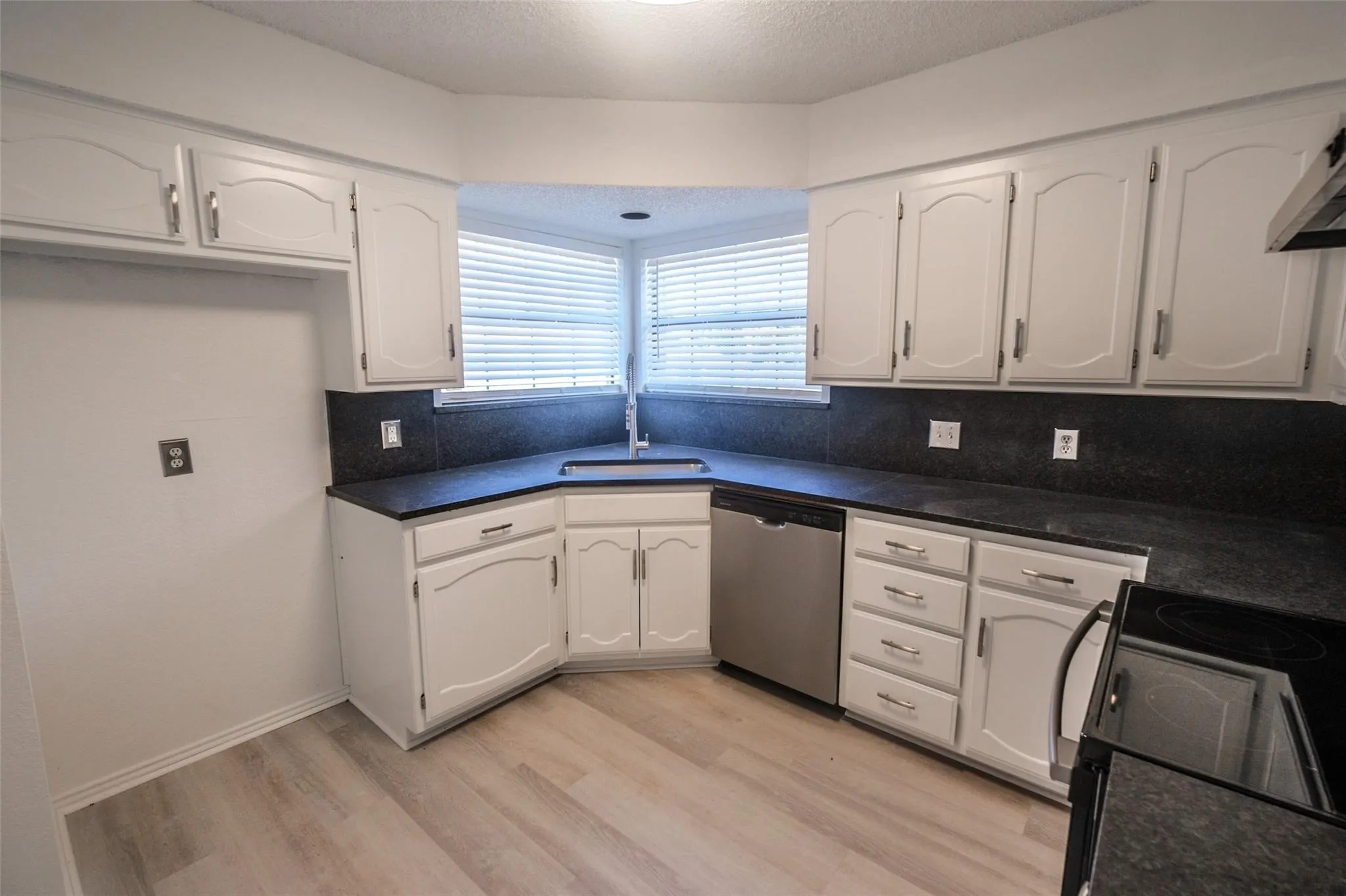 Kitchen featuring white cabinetry, dark countertops, wood-finish flooring, a stainless steel dishwasher, and a built-in electric stovetop