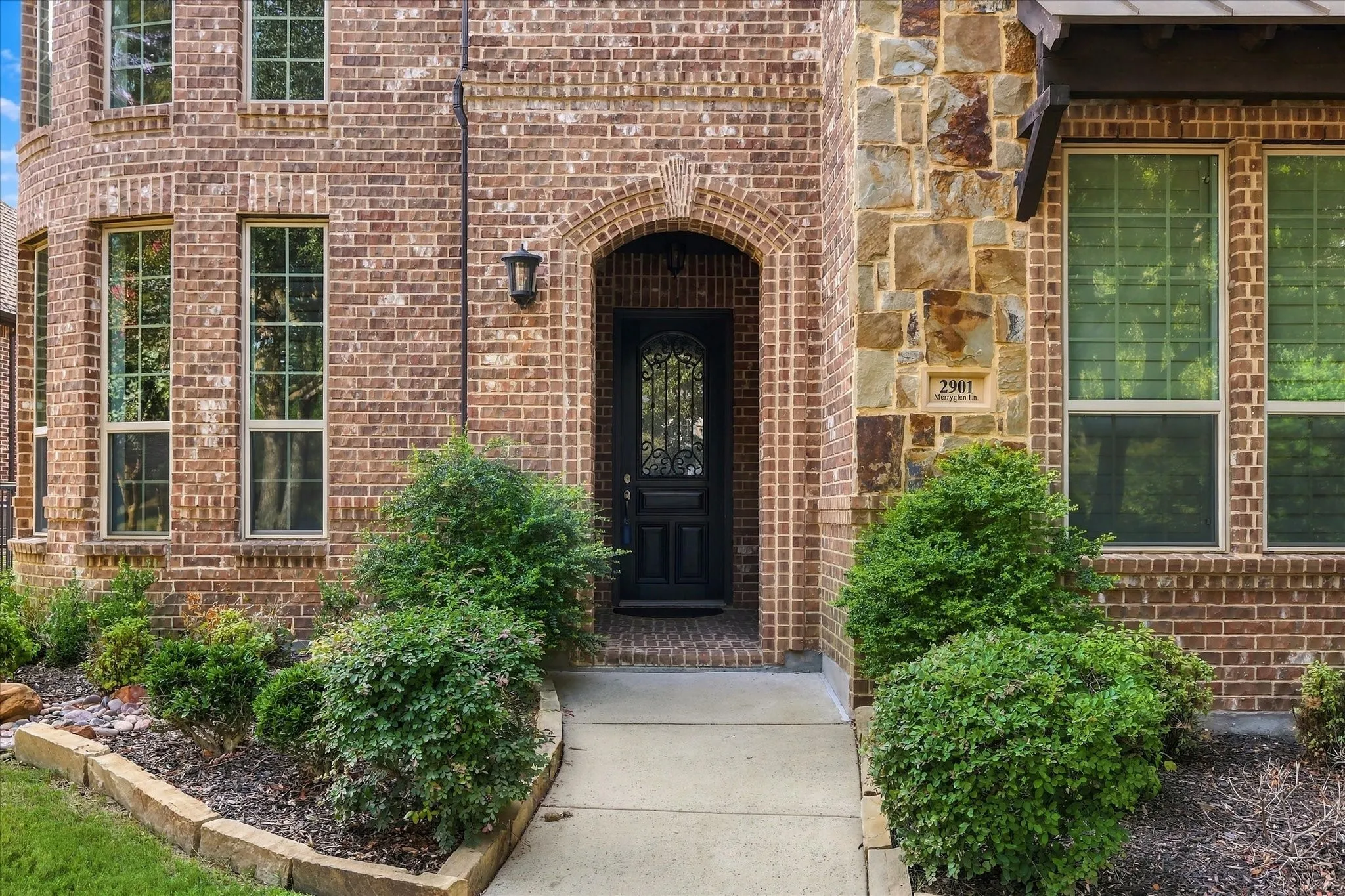 Brick and stone exterior with an arched entryway, decorative front door, and multiple windows