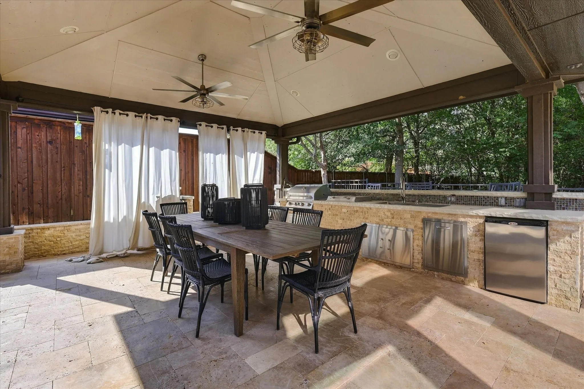 Covered outdoor patio with a vaulted ceiling, recessed lighting, and dual ceiling fans Outdoor kitchen grill and refrigerator.