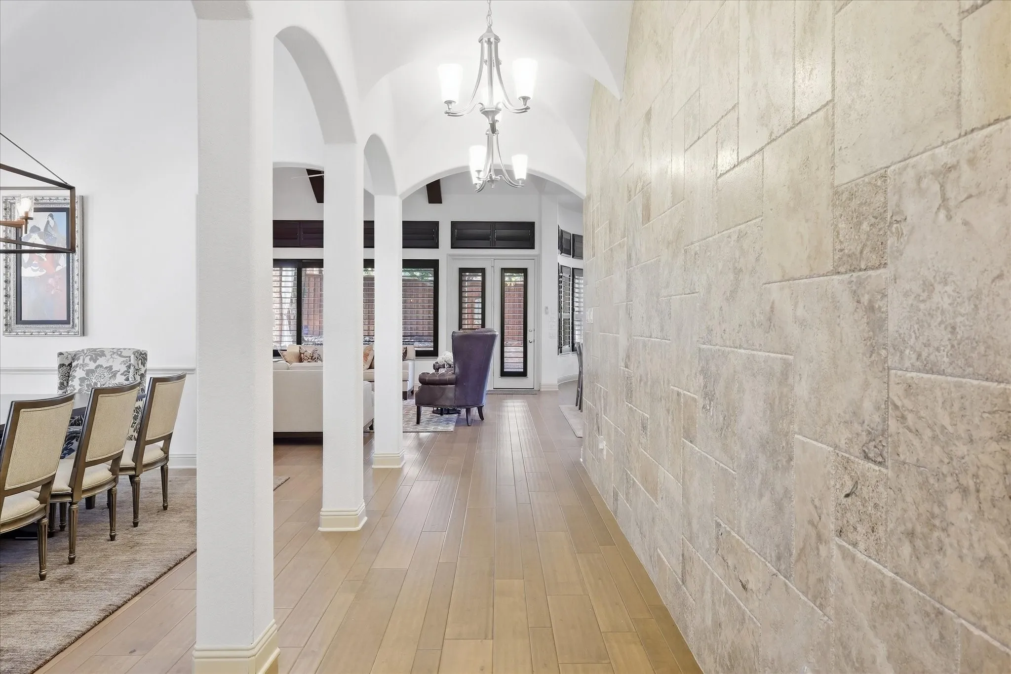Arched walkways, wood flooring, stone accent wall, and a vaulted ceiling with chandelier lighting