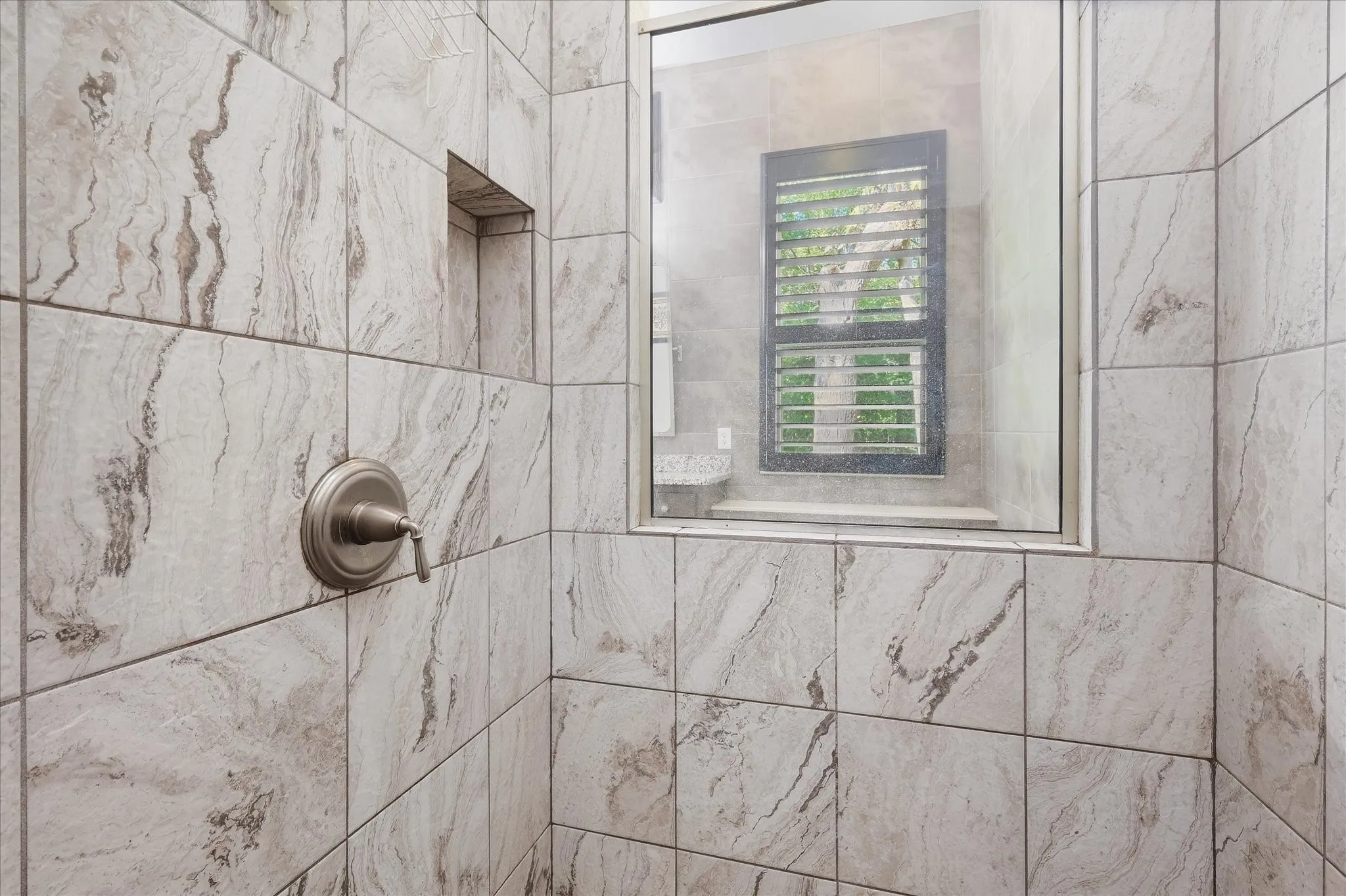 Walk-in shower with large format tile, built-in niche, and brushed nickel fixture