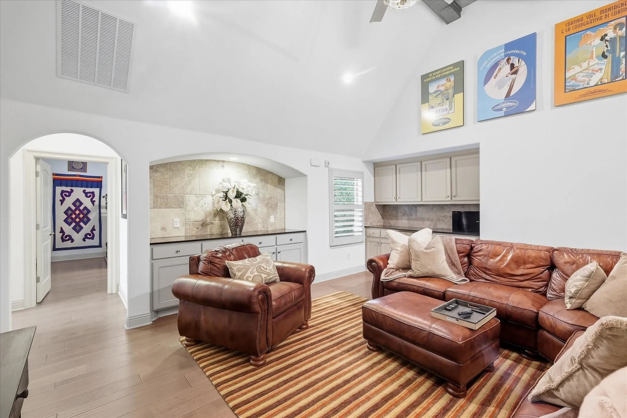 Vaulted ceiling with a ceiling fan, recessed lighting, wood-finish flooring, built-in cabinetry with stone countertops, and an arched entry