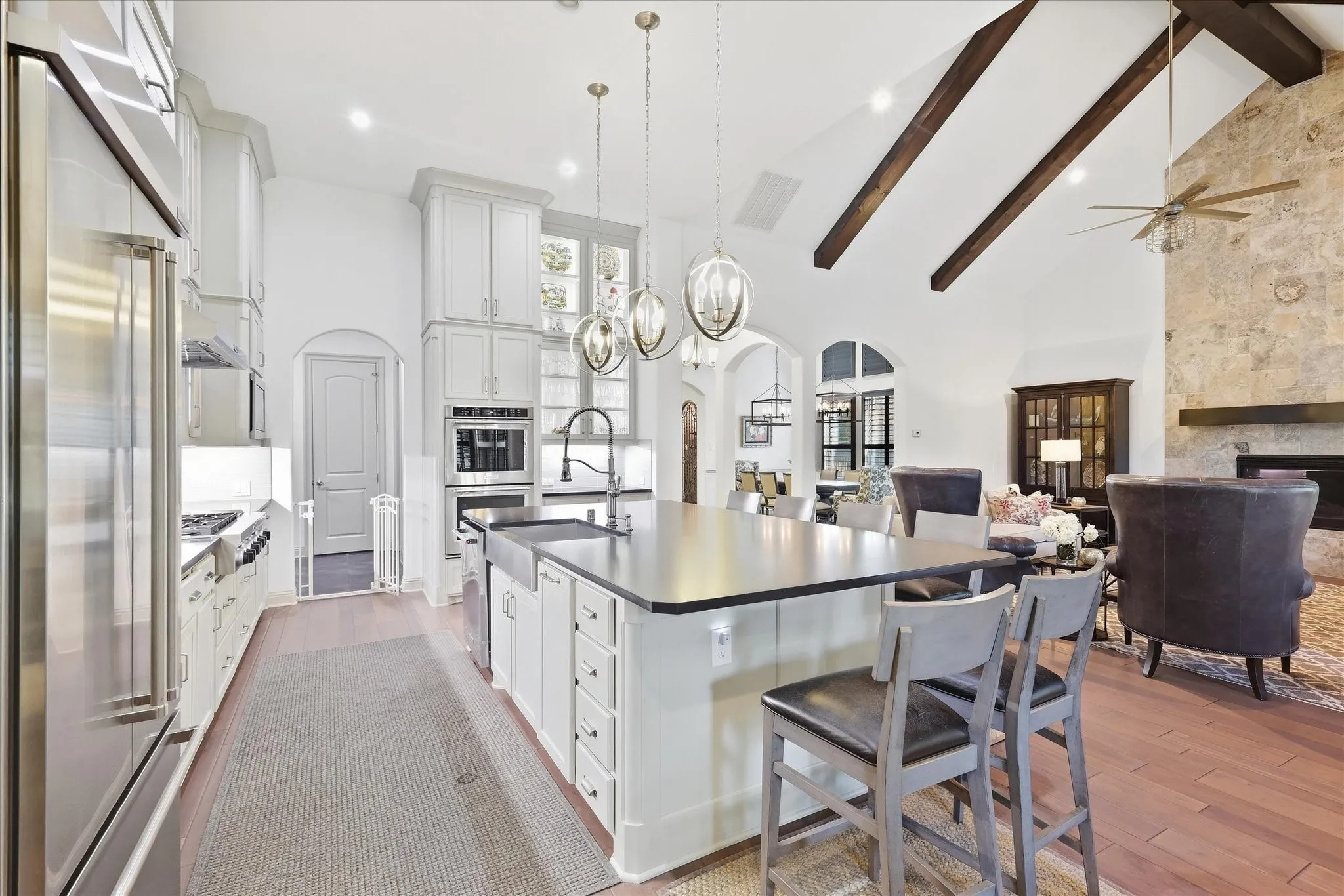 Kitchen island with seating, stainless steel appliances, vaulted ceiling with exposed beams, stone-clad fireplace, and wood-finish flooring