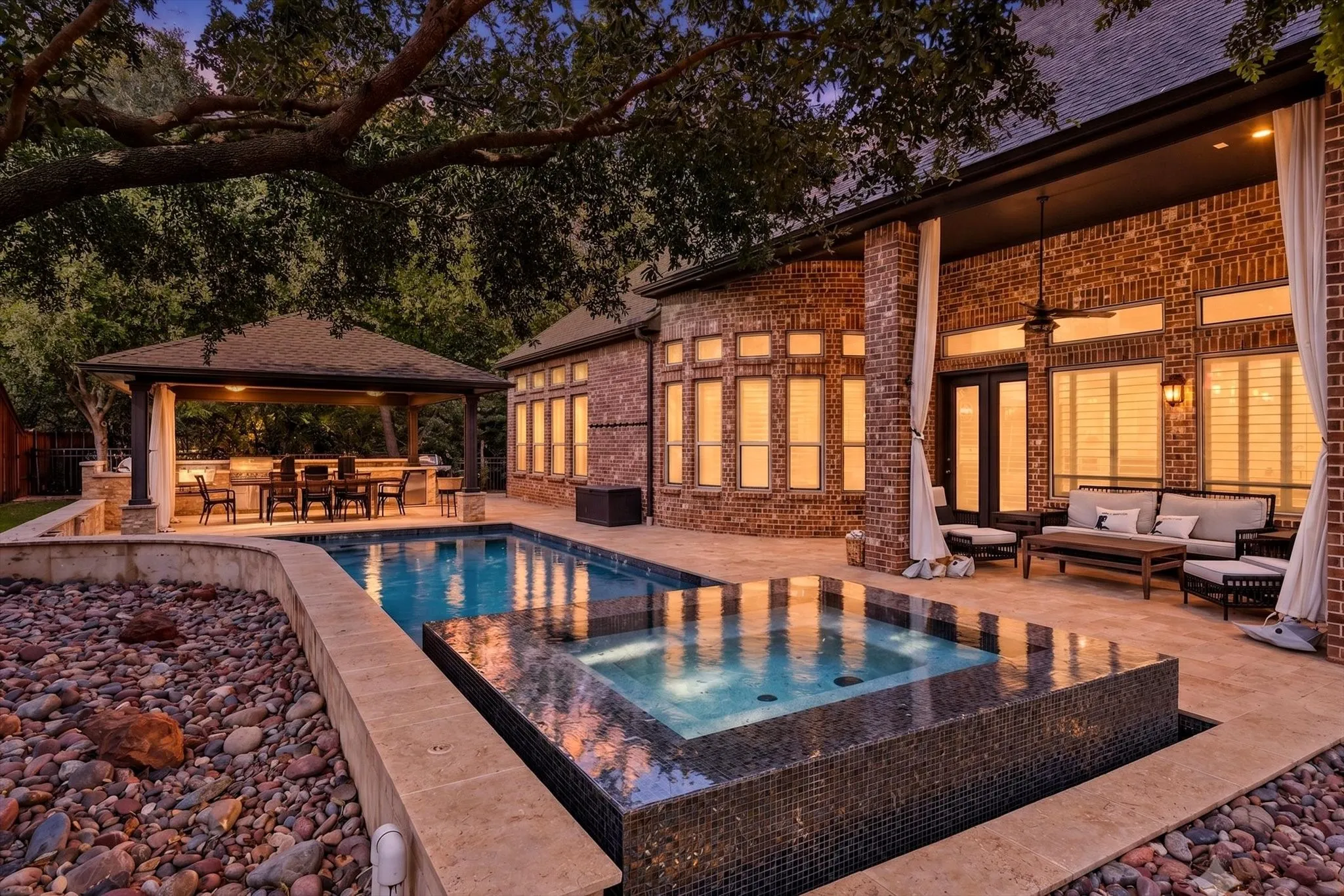 Brick exterior with a covered patio, outdoor ceiling fan, and extensive hardscaping