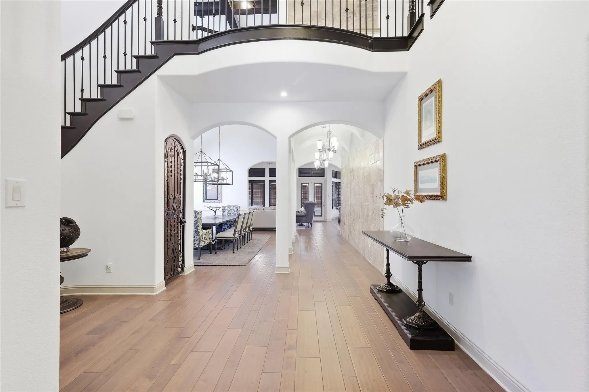 Grand entryway featuring light wood flooring, a sweeping staircase with wrought iron balusters, arched doorways, and recessed lighting