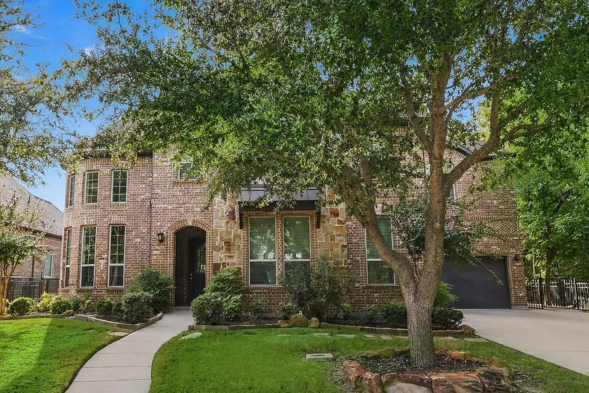 Brick and stone exterior featuring an arched entry, multiple windows, an attached garage, and a concrete pathway