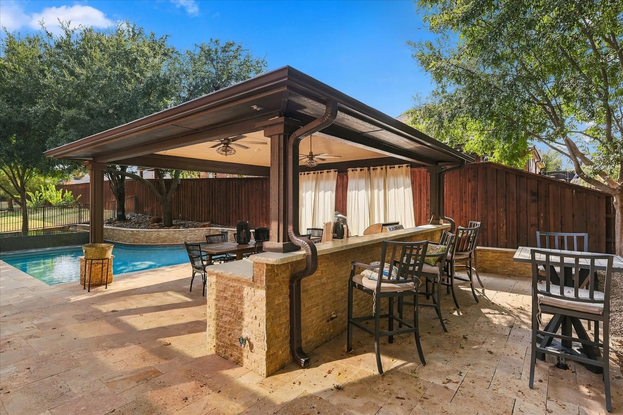 Expansive outdoor living area featuring a covered patio, built-in outdoor kitchen with bar seating, and a swimming pool