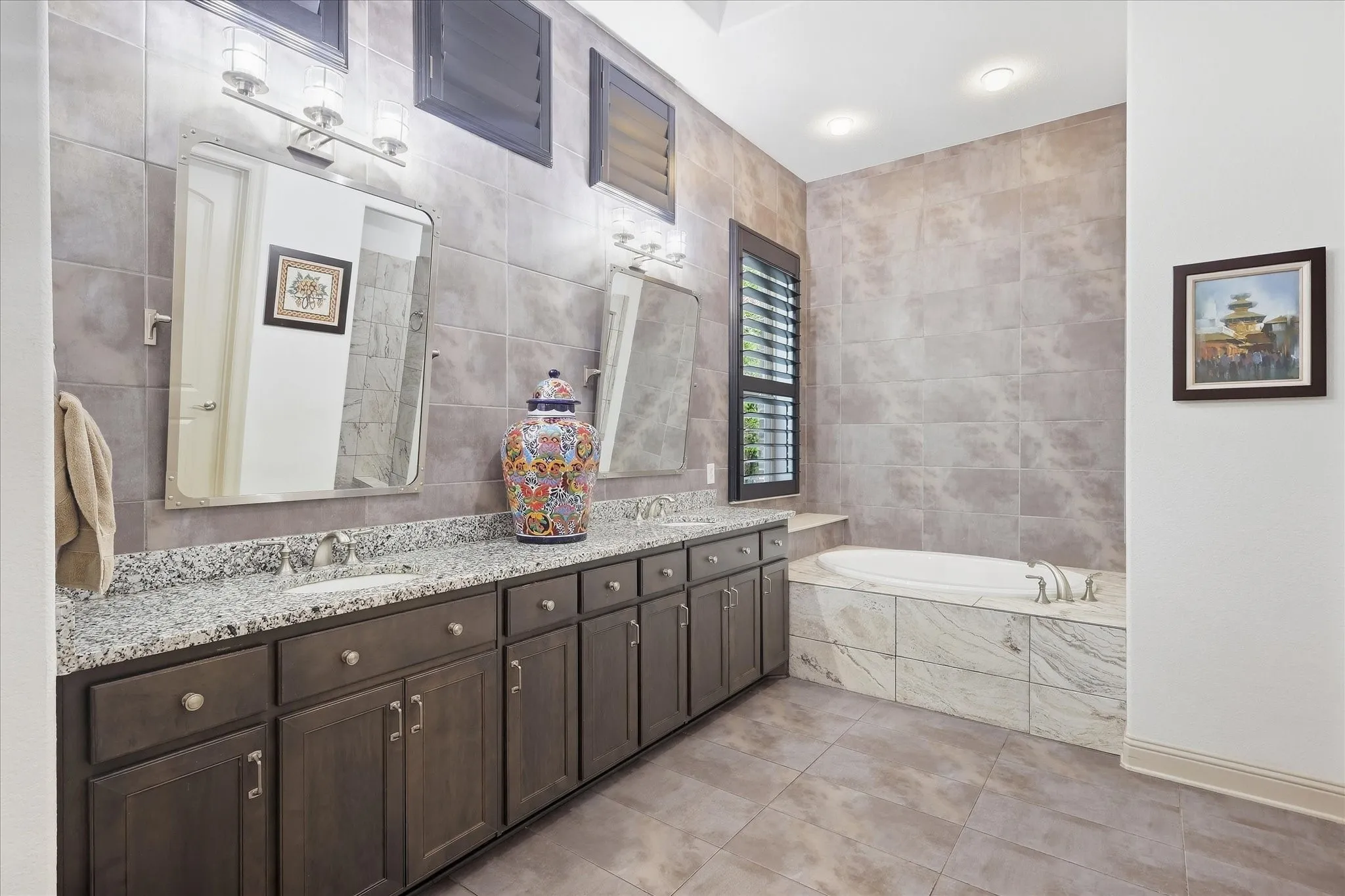 Double vanity with stone countertop, dark wood-finish cabinetry, tile flooring, built-in soaking tub, and tiled shower enclosure