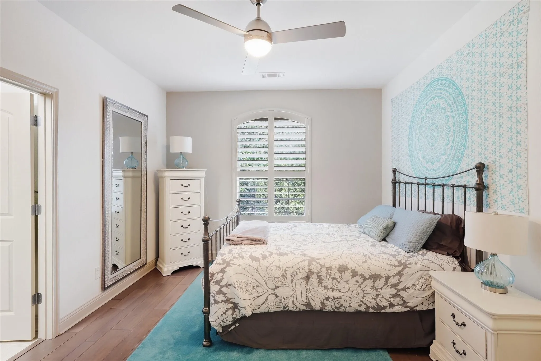 Hardwood flooring, arched window with plantation shutters, ceiling fan with integrated lighting, and a solid core door
