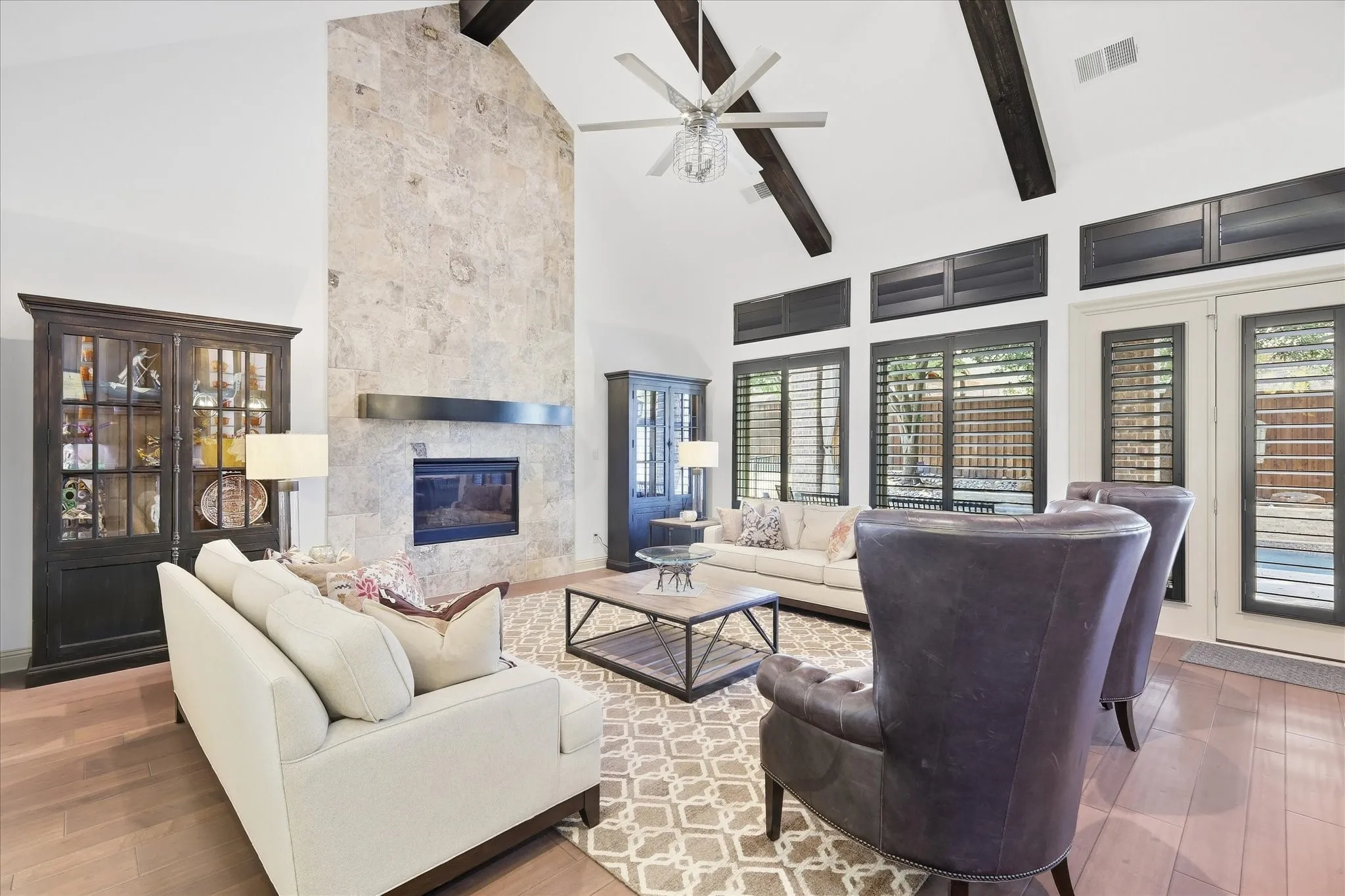 Vaulted ceiling with exposed wood beams, floor-to-ceiling stone fireplace, gas insert, and wood flooring