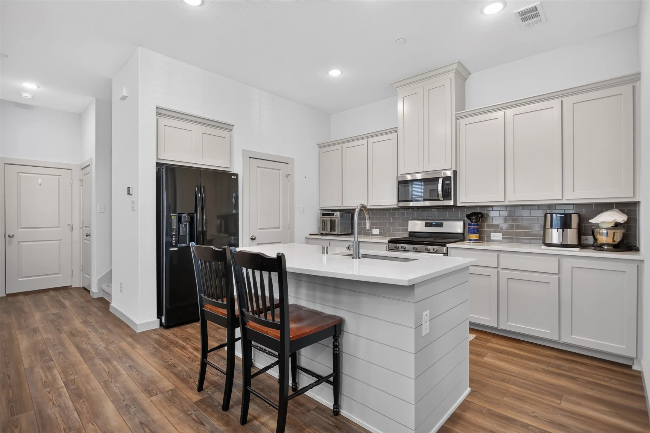 Kitchen featuring wood-finish flooring, an island with shiplap detailing and countertop seating, light-toned cabinetry, stainless steel appliances, and subway tile backsplash