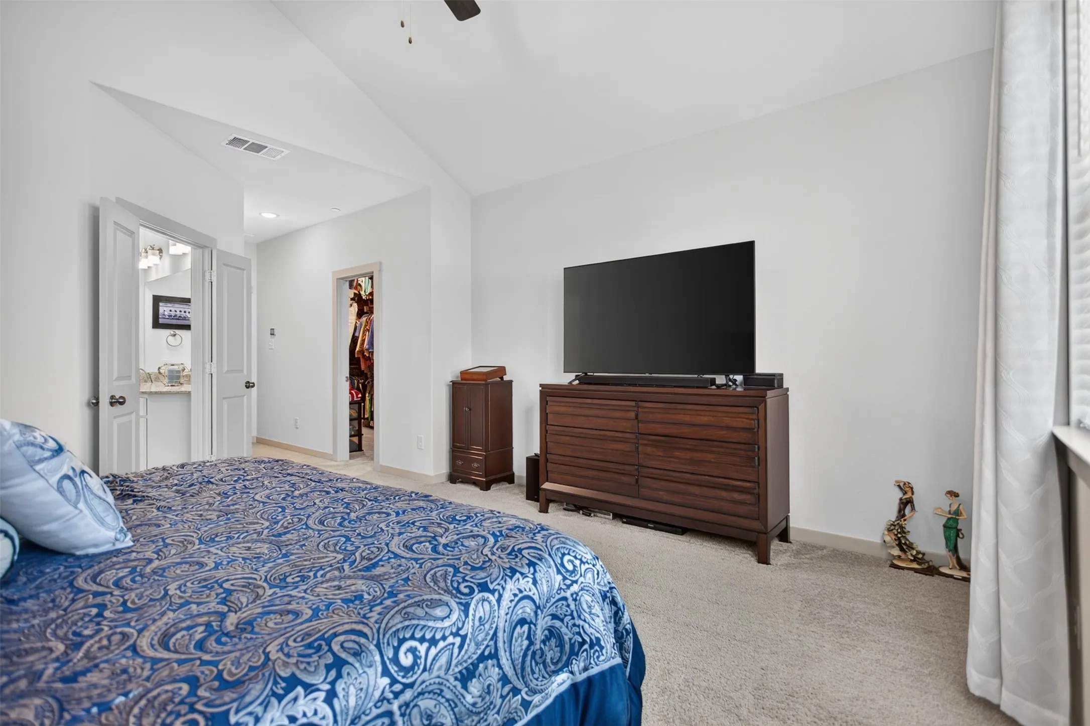Vaulted ceiling, ceiling fan, white walls, light-colored carpeting, and a built-in vanity with dual sinks