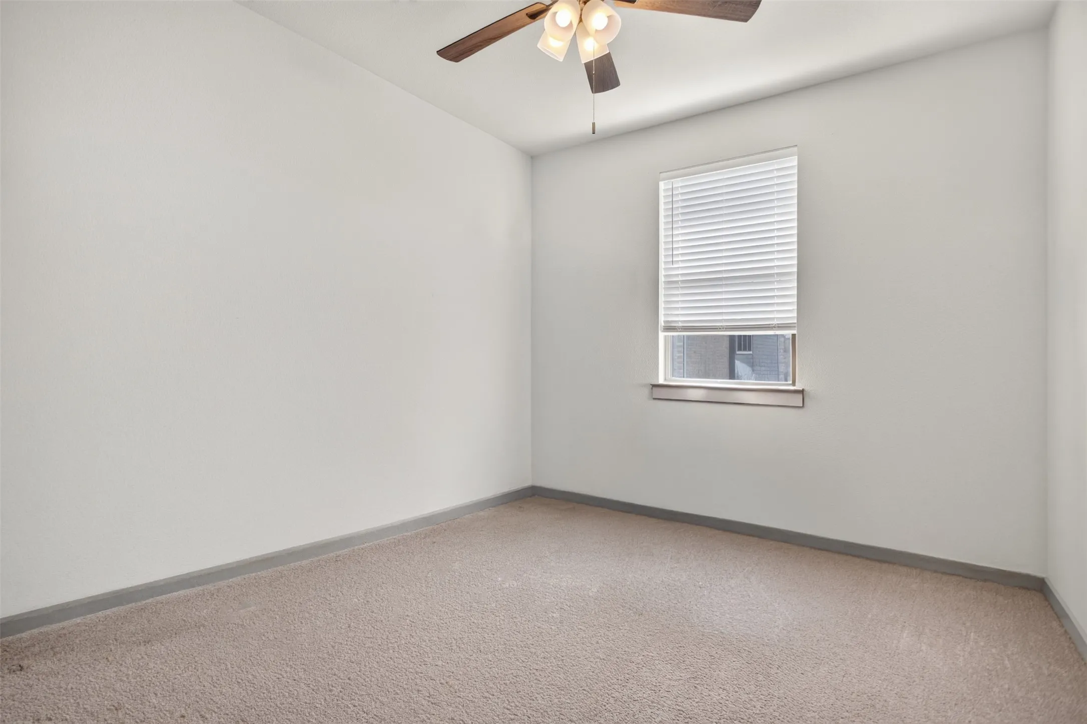 Neutral wall color, carpeted flooring, window with blinds, and a ceiling fan with integrated lighting
