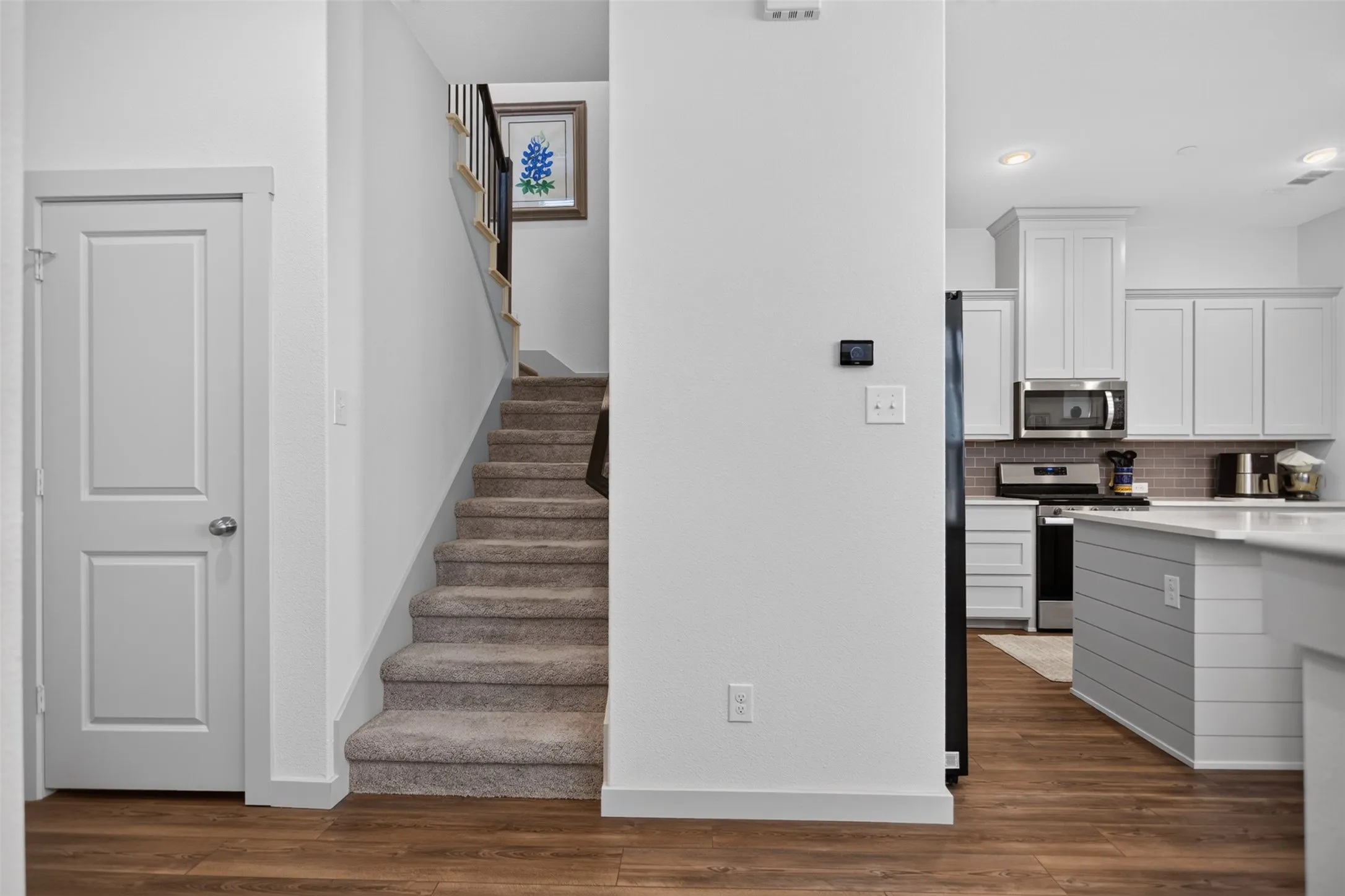 Wood-finish flooring, white paneled doors, carpeted staircase, and a kitchen featuring white cabinetry and stainless steel appliances