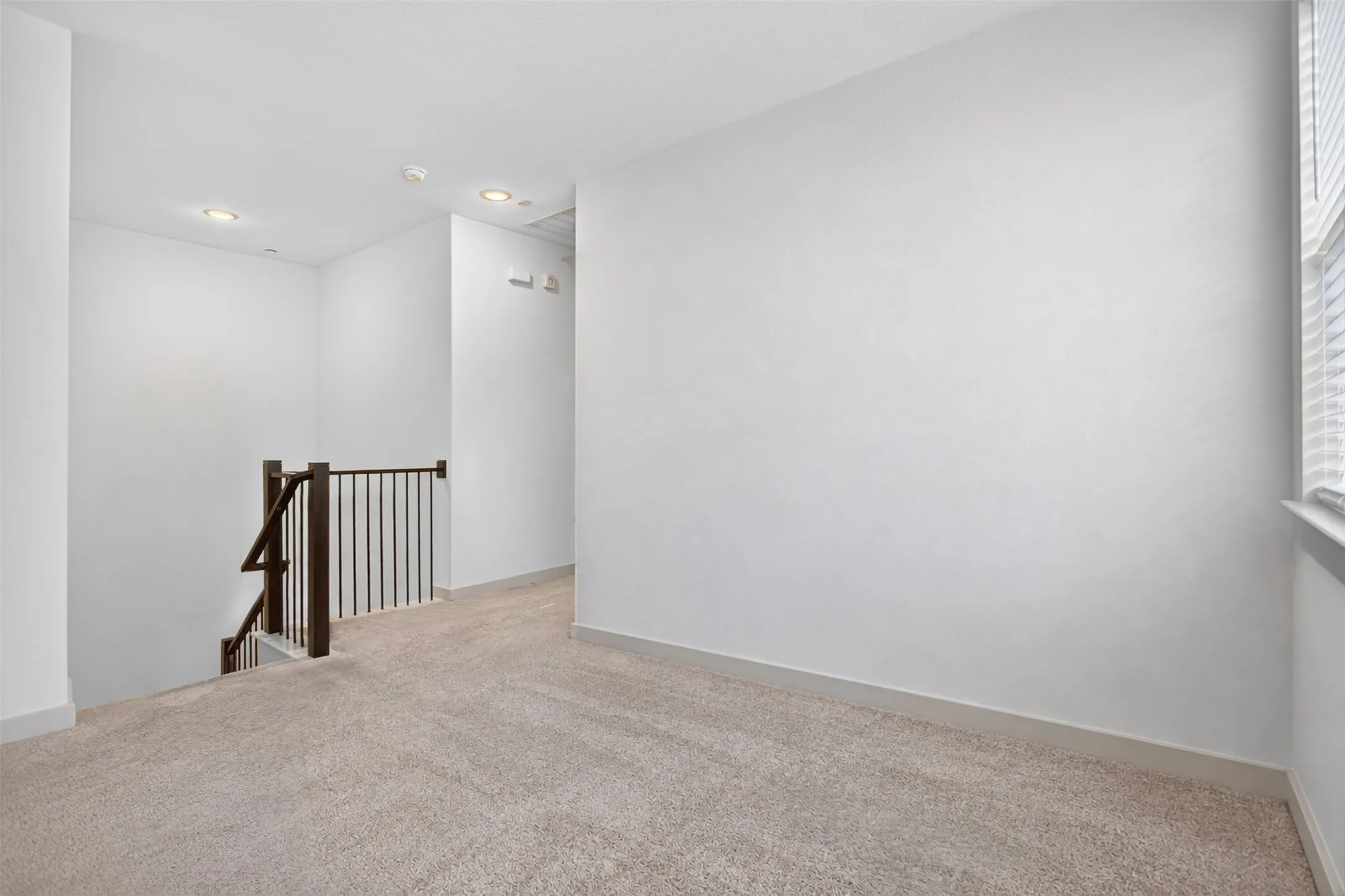 Carpeted landing with recessed lighting, a dark wood newel post, and metal balusters