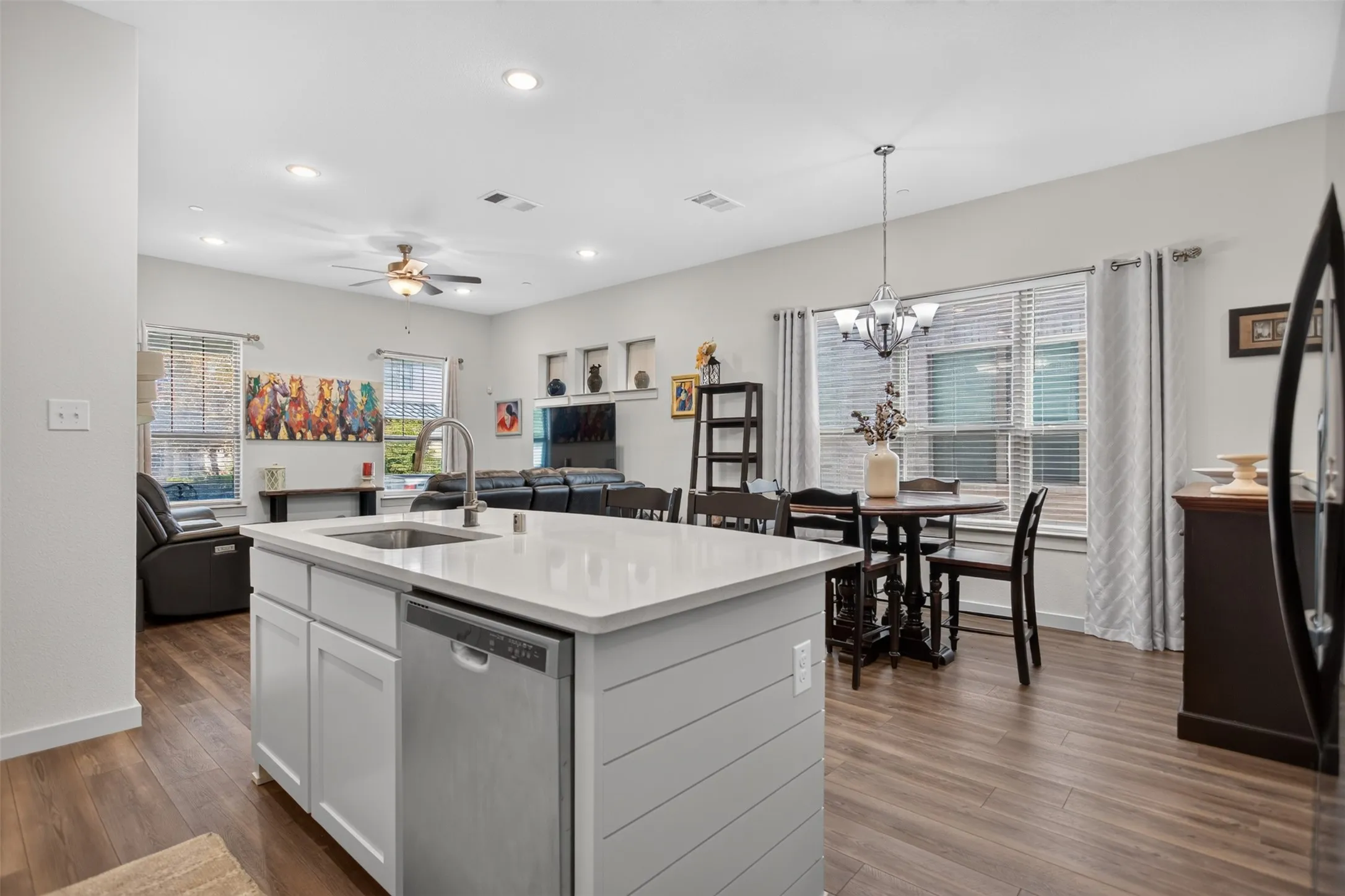 Open-concept living area featuring a kitchen island with sink and integrated dishwasher, wood-finish flooring, recessed lighting, and a ceiling fan