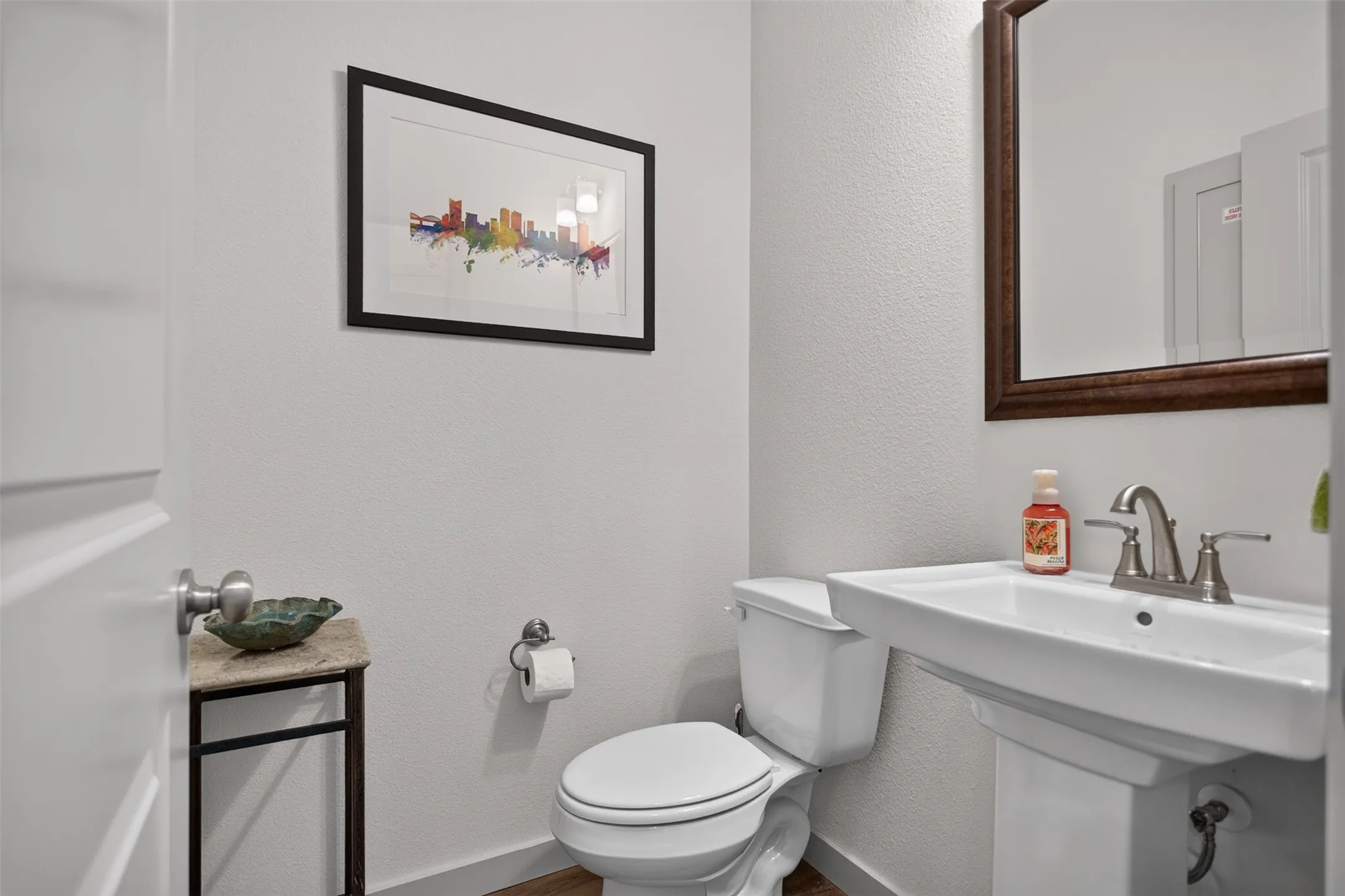 White pedestal sink with brushed nickel faucet, framed mirror, and wood-finish flooring