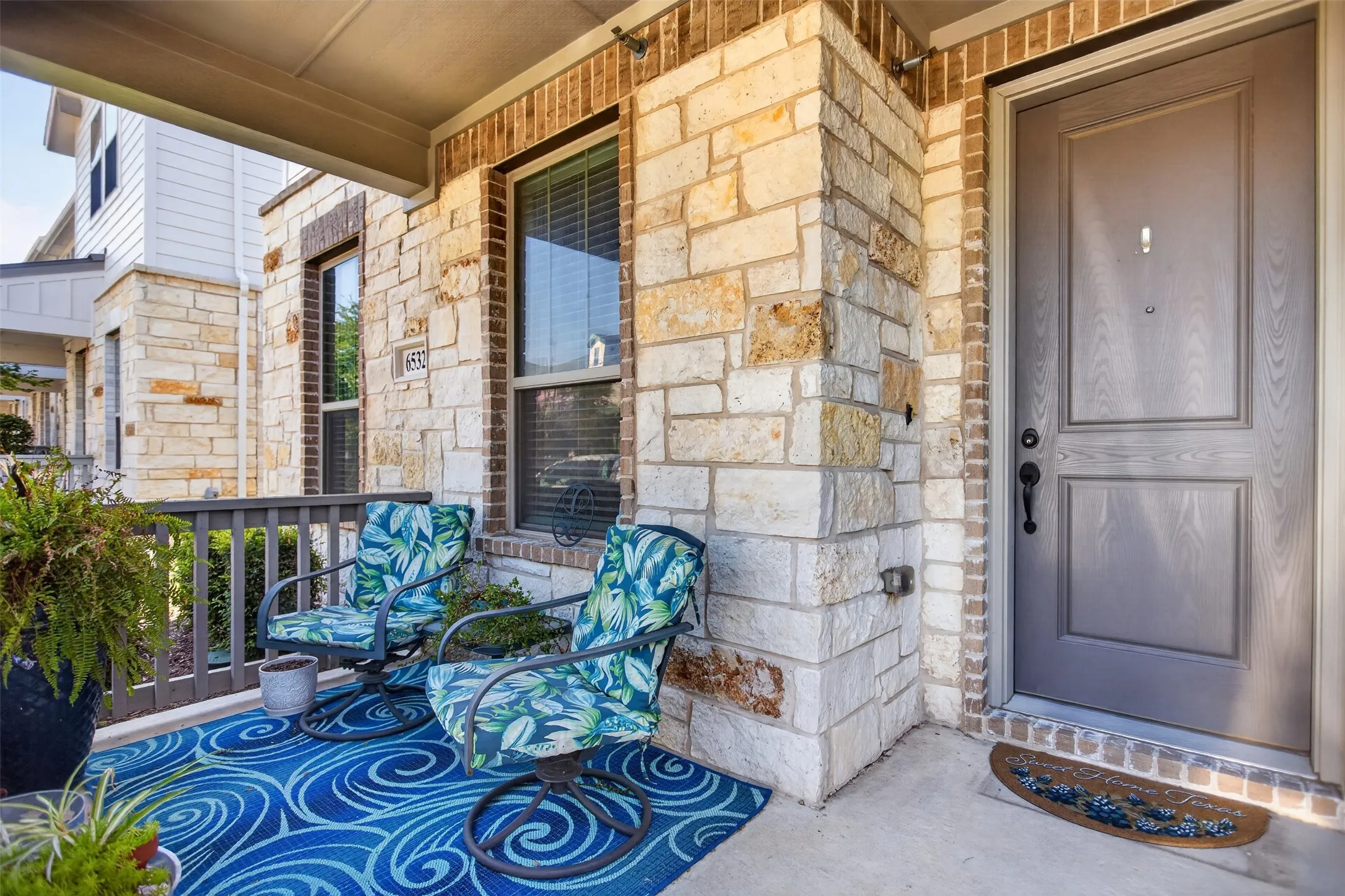Covered front porch featuring a paneled entry door, stone and brick facade, and wood railing