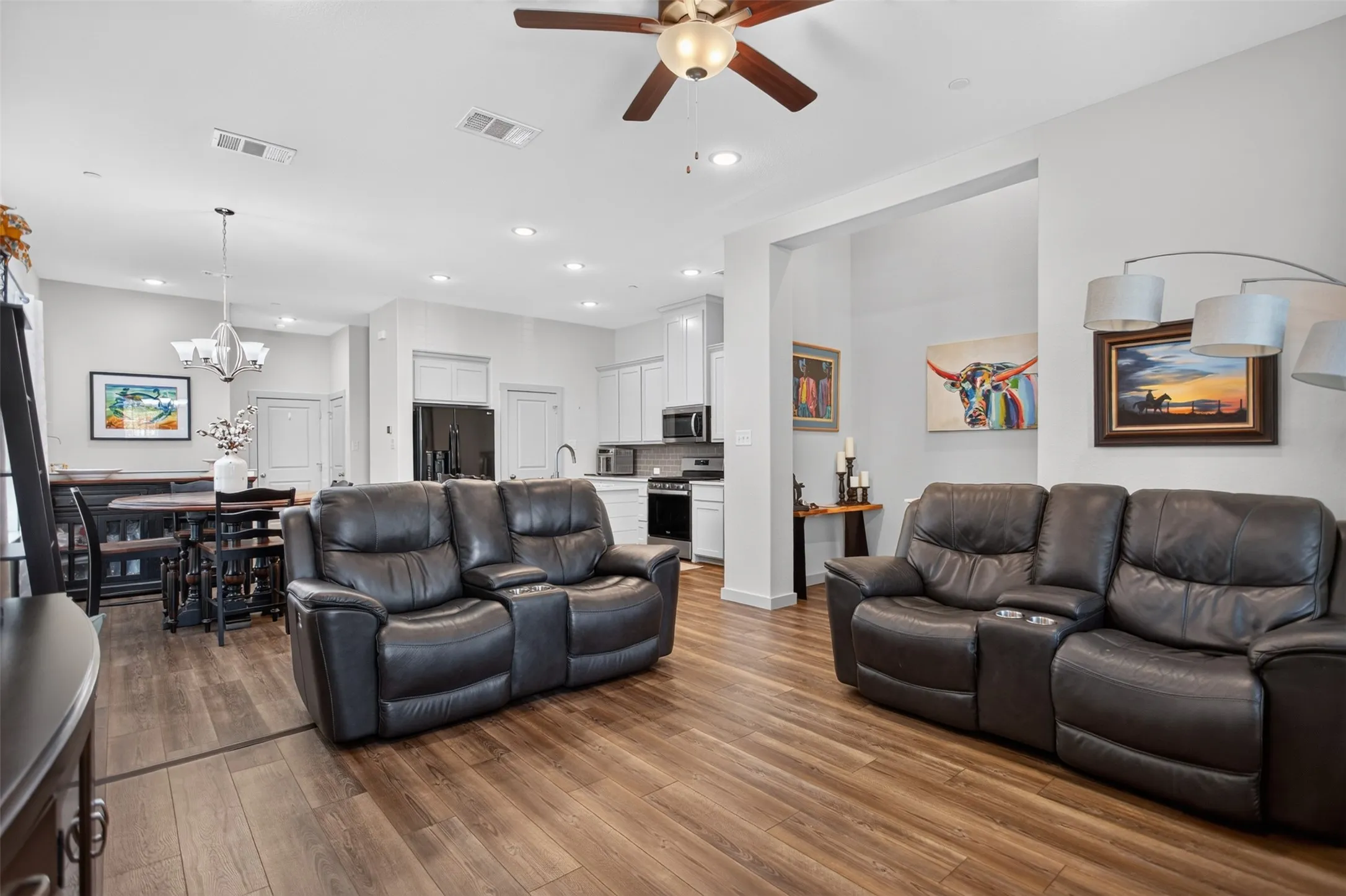 Open-concept living area with wood-finish flooring, ceiling fan, recessed lighting, and a kitchen featuring white cabinetry and black appliances