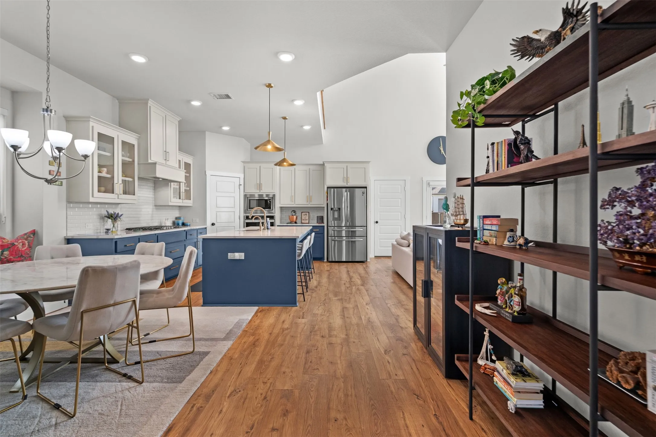 Kitchen featuring a vaulted ceiling, wood-finish flooring, two-tone cabinetry with glass-front uppers, a full-size refrigerator, and a kitchen island with seating