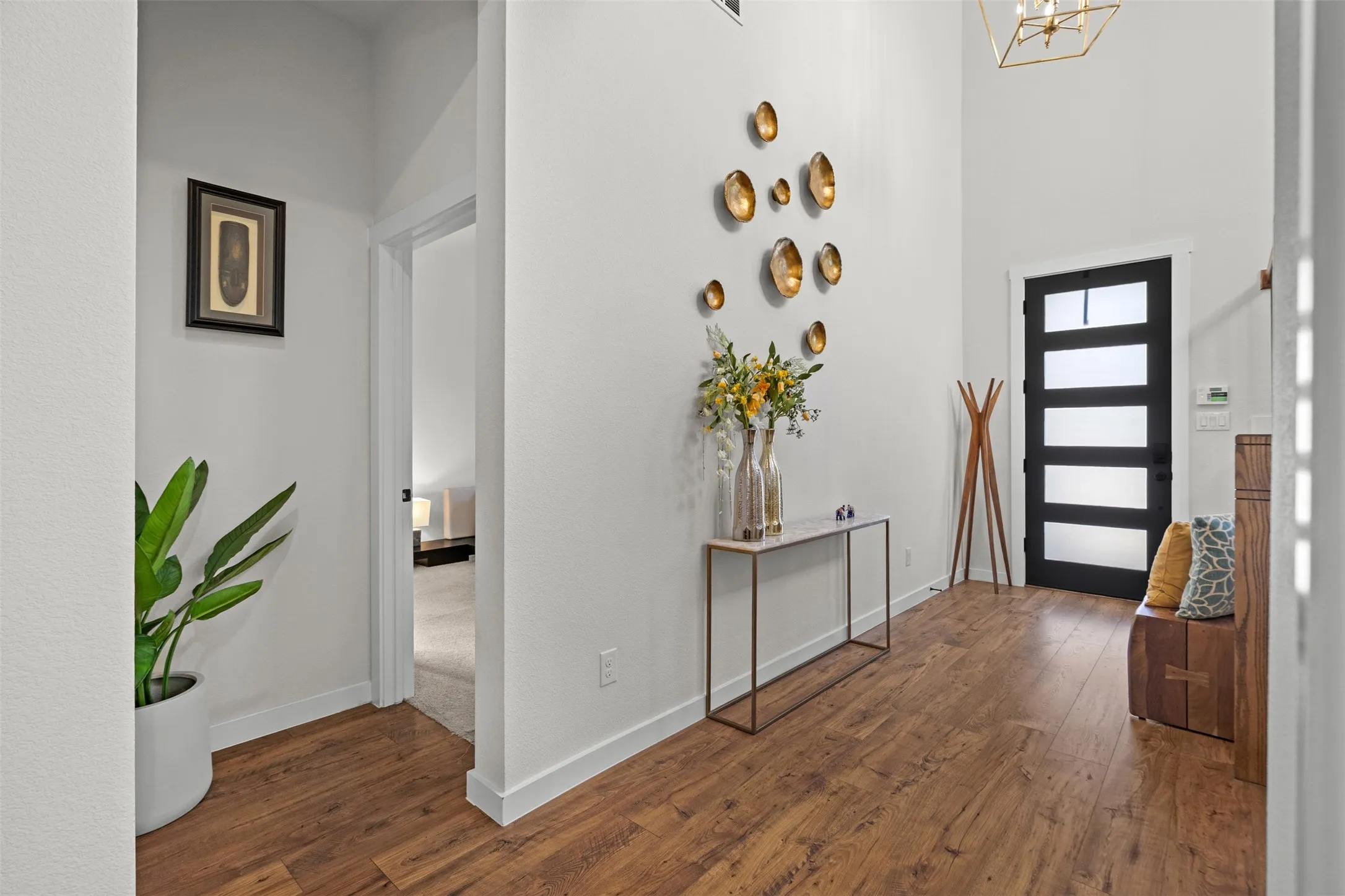 Vaulted entry with wood-finish flooring, a modern black paneled entry door, and a brass-tone chandelier