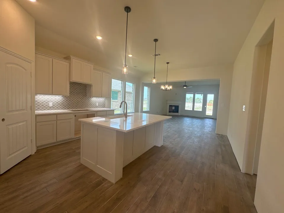 Kitchen featuring a large island with sink, white shaker cabinetry, patterned tile backsplash, and wood-finish flooring