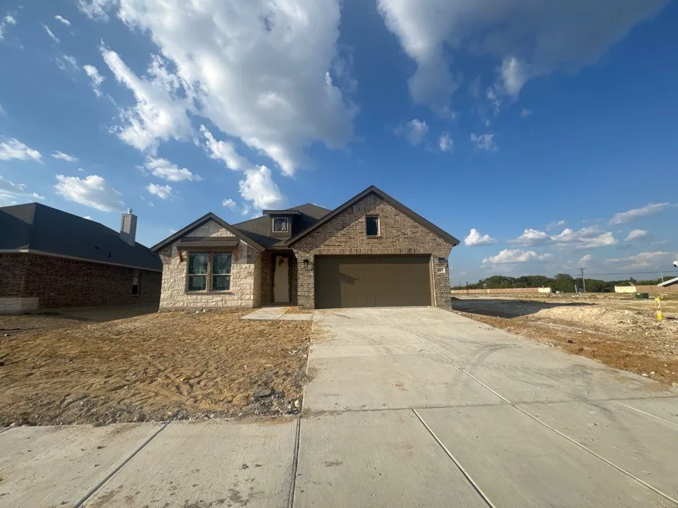 Brick and stone exterior with a gabled roofline, concrete driveway, and attached garage