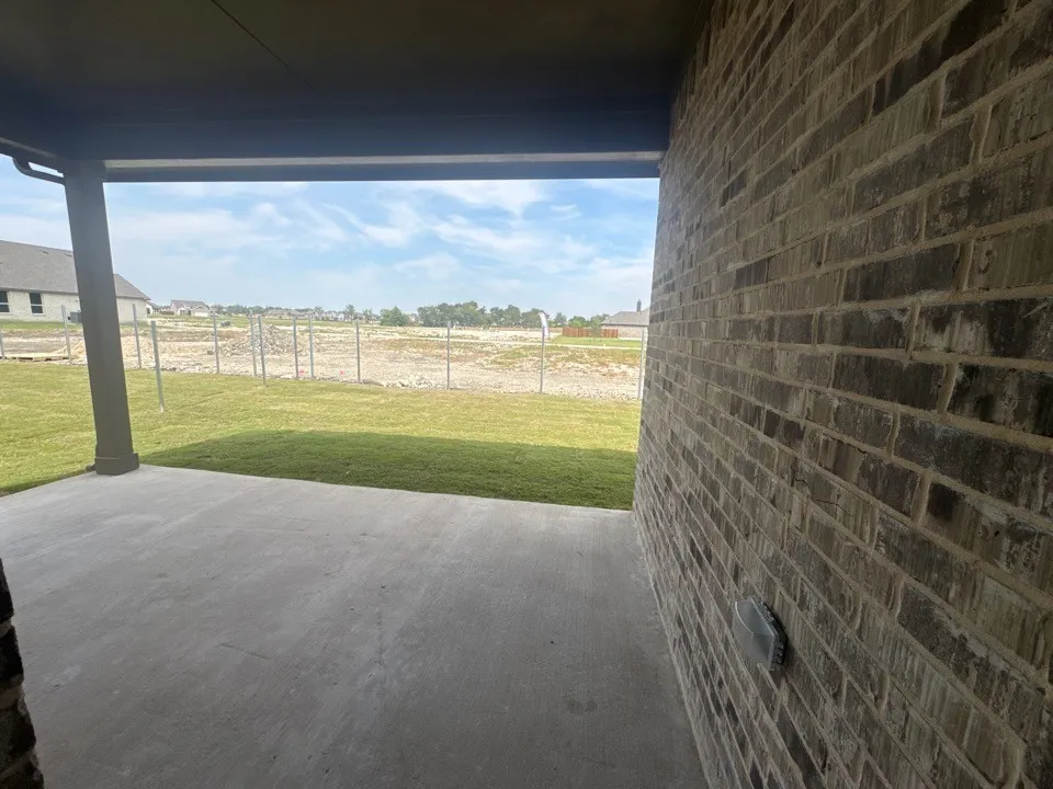 Covered concrete patio with brick exterior and a green lawn