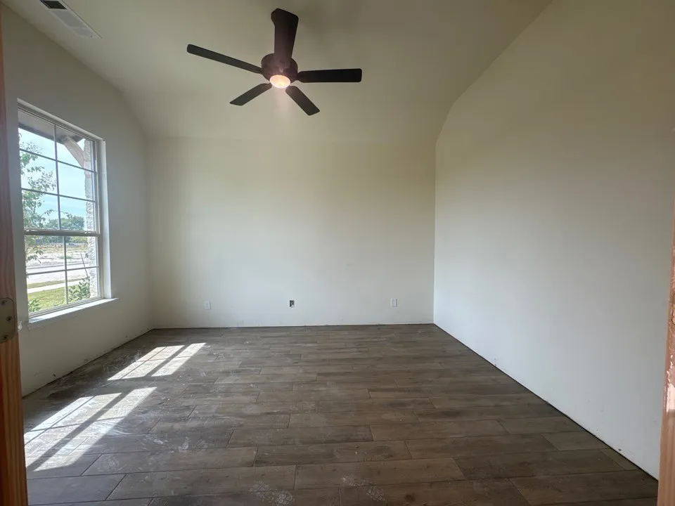Vaulted ceiling, wood-finish flooring, ceiling fan with integrated lighting, and a large window