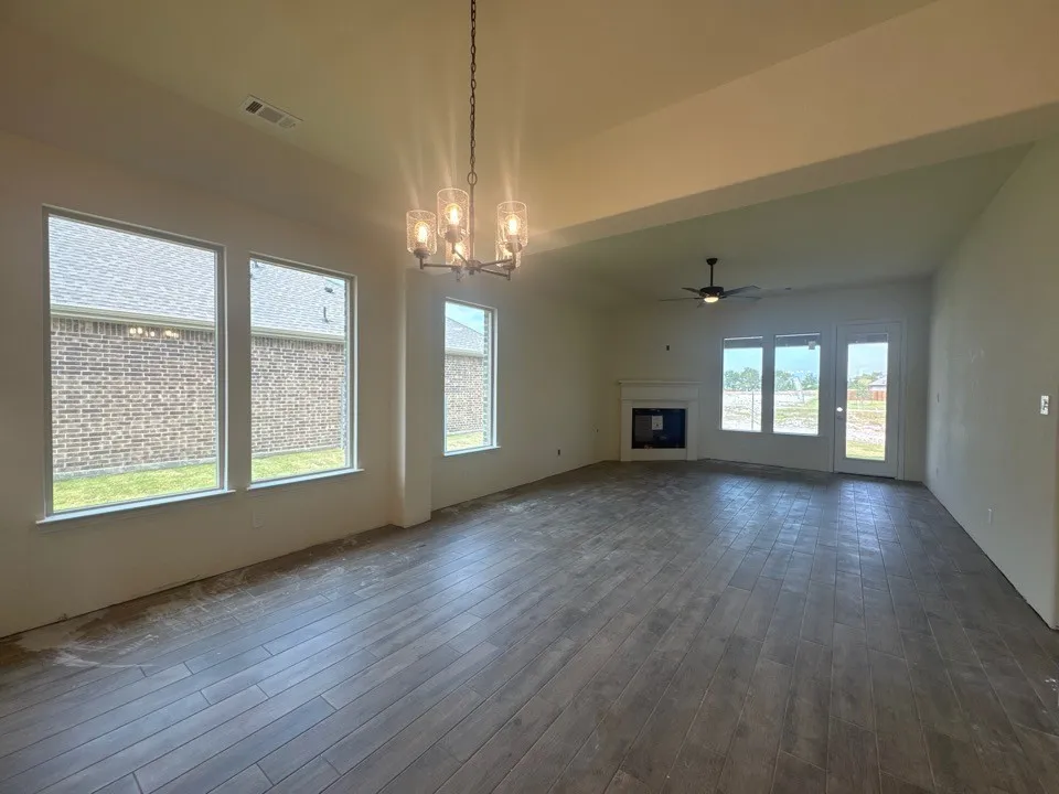 Spacious interior featuring wood-finish flooring, multiple windows, a ceiling fan, and a fireplace with a white mantel