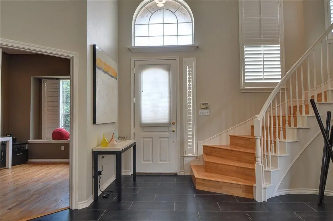Entryway featuring dark tile flooring, a curved staircase with wood-finish treads and white risers, and a prominent arched transom window above the entry door