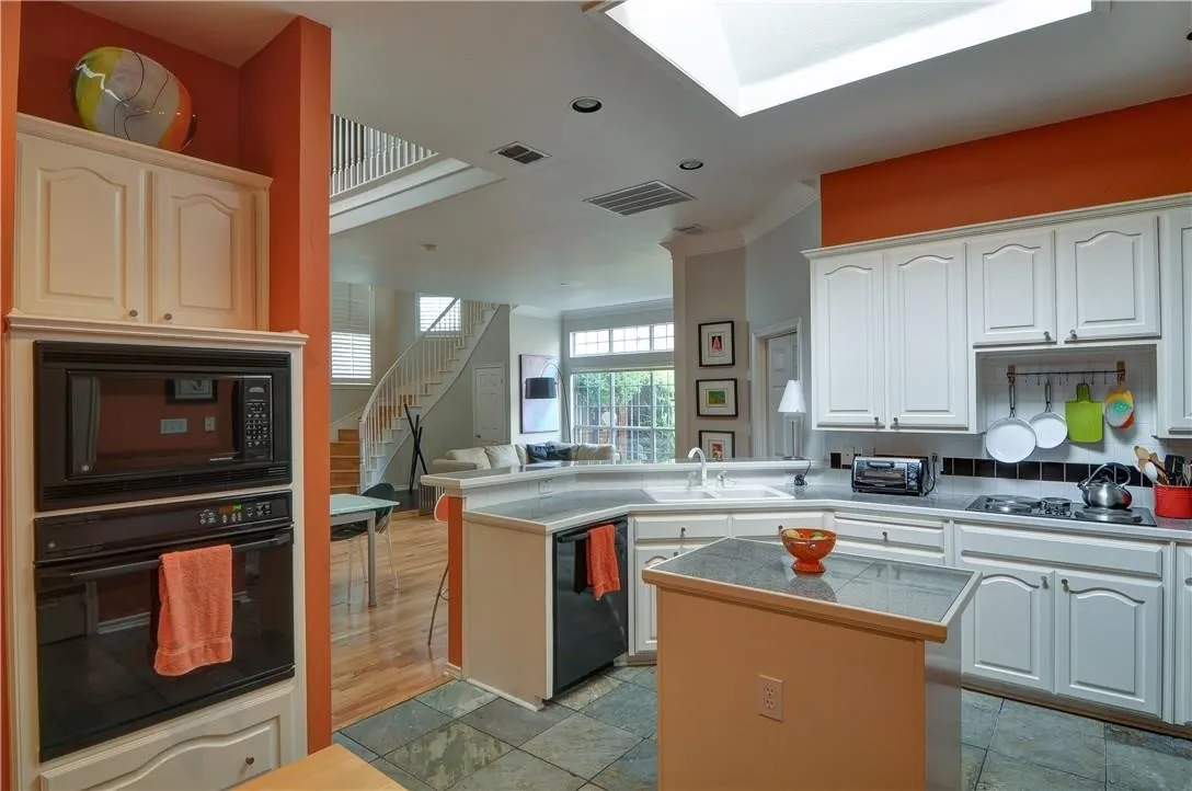 Kitchen featuring white cabinetry, built-in wall oven and microwave, skylight, and stone-finish flooring