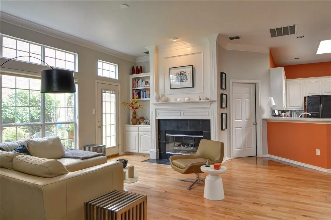 Hardwood flooring, large windows with transom lighting, built-in shelving, a fireplace with a tile surround, and a kitchen pass-through