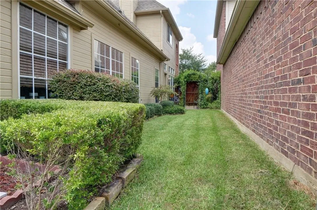 Side yard with a manicured lawn, established shrubbery, and a decorative garden gate