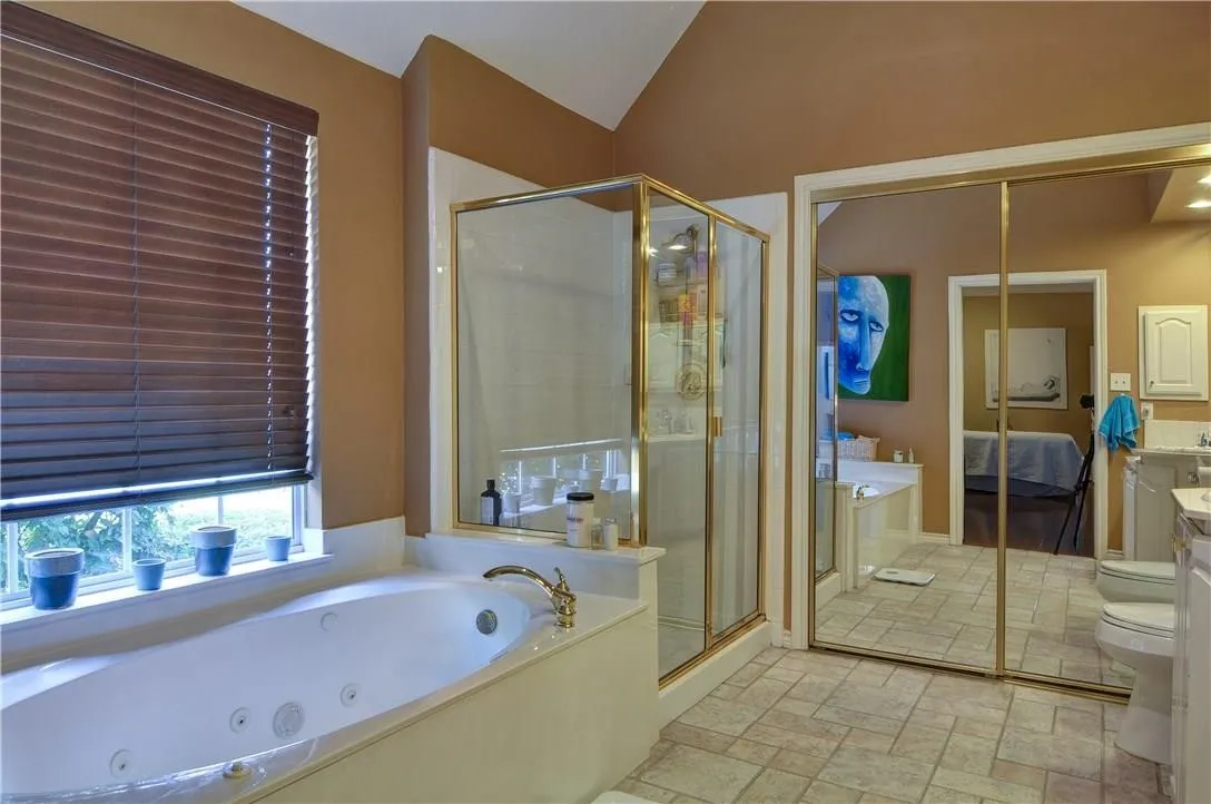 Integrated soaking tub with brass-finish fixtures, glass-enclosed shower with brass-finish framing, mirrored wardrobe doors, and tiled flooring