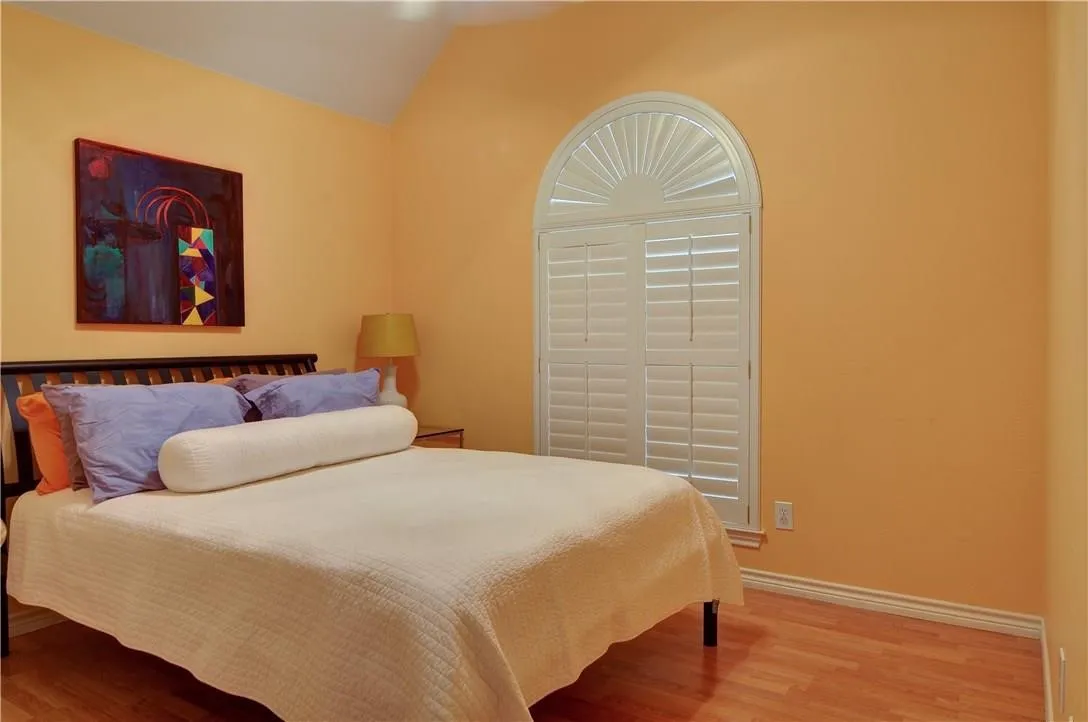 Arched window with plantation shutters, wood-finish flooring, and a vaulted ceiling