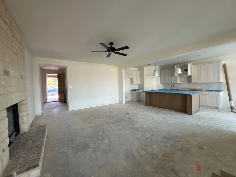Stone fireplace with hearth, ceiling fan, white upper and lower cabinetry, kitchen island with wood-finish base, pendant lighting