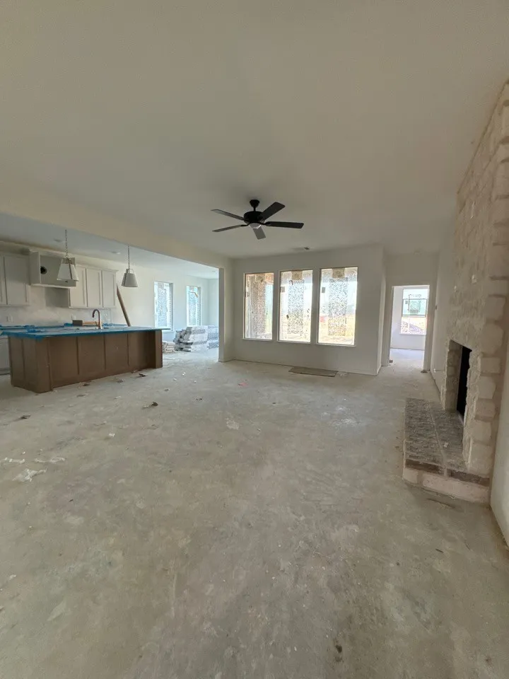 Stone-faced fireplace with brick hearth, ceiling fan with matte black finish, multiple windows, kitchen island with wood-finish cabinetry, and recessed lighting