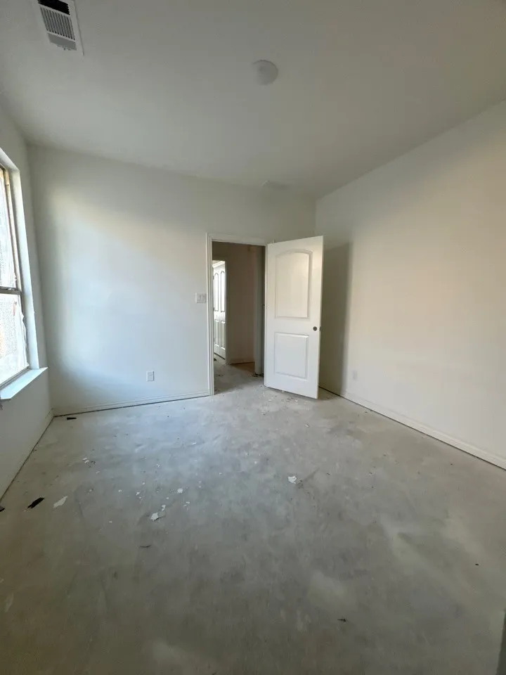 Recessed ceiling lighting, white interior door, window opening, white walls, and concrete flooring