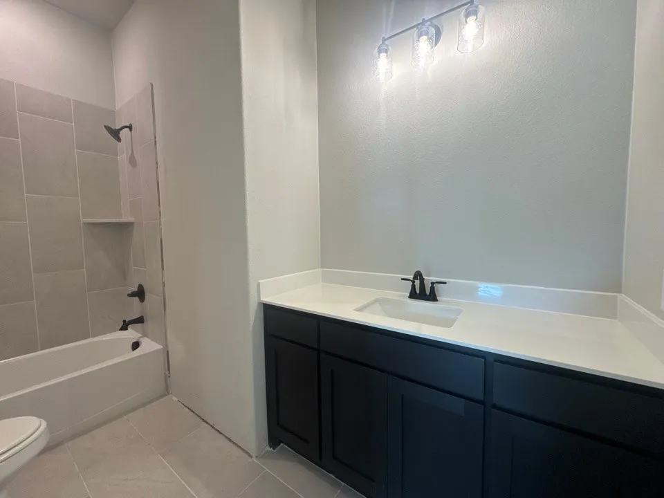 Black vanity with a white countertop and integrated sink, matte black faucet, and three-light vanity fixture