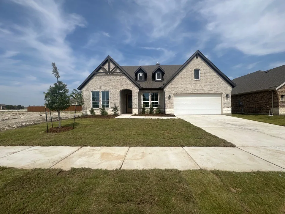 Brick facade with dark trim accents, dormer windows, attached garage, and a concrete driveway