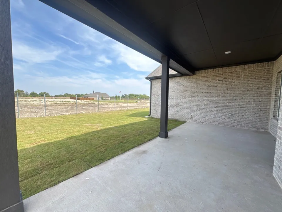 Covered patio with a concrete surface, gray brick exterior, and a manicured lawn