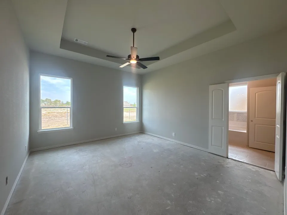 Tray ceiling with a ceiling fan, two windows, and double doors to an adjoining room