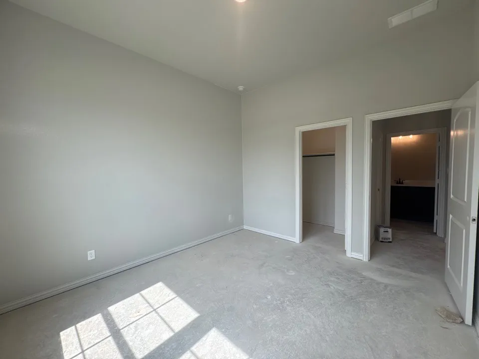 Spacious room with light gray wall paint, an open closet, and an adjacent bathroom featuring a dark vanity with a white countertop