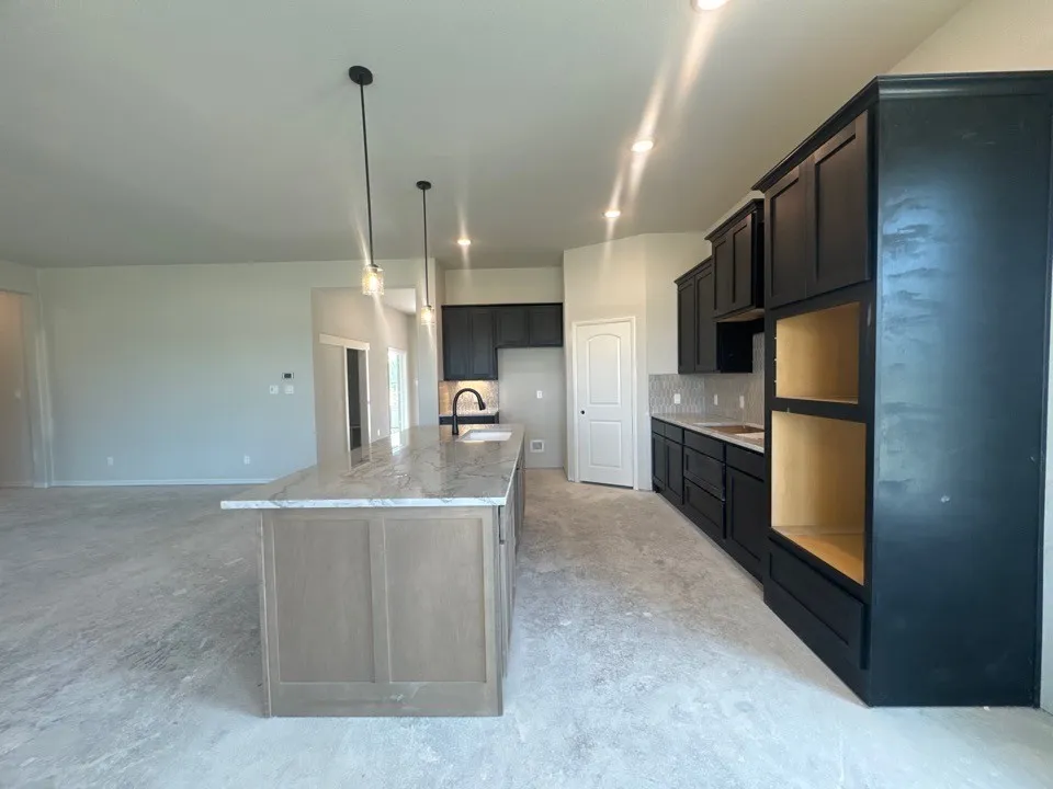 Kitchen featuring a central island with a light-toned countertop, black cabinetry, a white tile backsplash, and recessed lighting