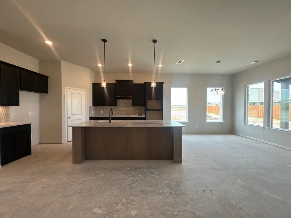 Kitchen island with pendant lighting, dark wood-finish cabinetry, light-toned countertops, tile backsplash, and recessed lighting